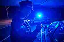 Dieses Bild zeigt einen Polizeivollzugsbeamten bei einer Verkehrskontrolle in Dunkelheit. Im Hintergrund ist das Blaulicht des Funkstreifenwagens zu sehen.