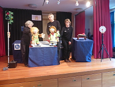 Bild zeigt die Handspielpuppen und ihre Spielerinnen und Spieler. Zu sehen sind die Puppen KAI (Herr Rosenberg) und MIA (Frau Müller) und der Drache REXI (Frau Ellermann-Rosenberg)