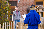 Eine Person in einer Arbeitshose steht vor dem Garten und spricht mit einer älteren Dame