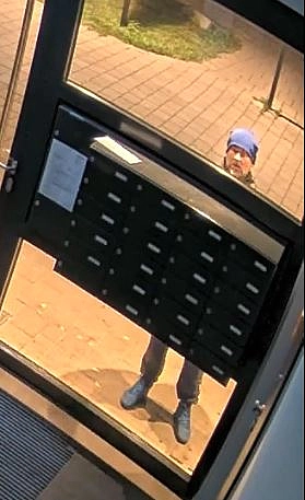 Auf dem Bild ist der Tatverdächtige vor den Briefkästen des Hauses zu sehen.