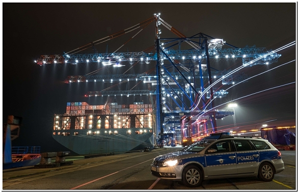 Das Bild zeigt einen Streifenwagen im Bereich eines Containerhafens bei Nacht.