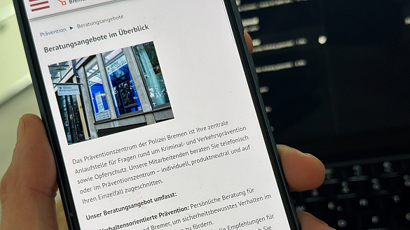 Hand,  die ein Handy hält auf der die Homepageseite des Präventionszentrums der Polizei Bremen abgebildet ist.