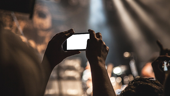 Person steht in einer Menschenmenge und hält ein Smartphone hoch
