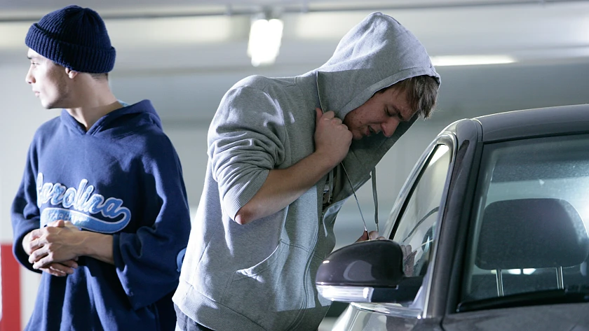 Zwei junge Männer, die an einem Fahrzeug stehen. Einer schaut in das Fahrzeuginnere, der andere steht augenscheinlich Schmiere 