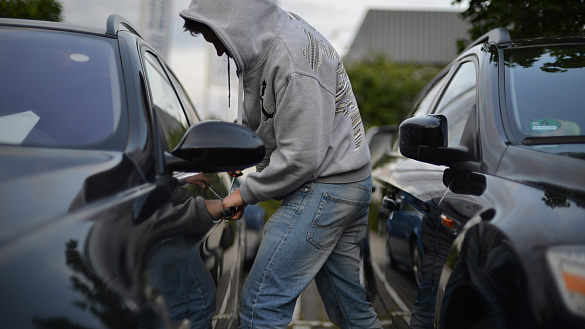 Vermummte Person, die mit einem Schraubendreher an einer Autotür manipuliert