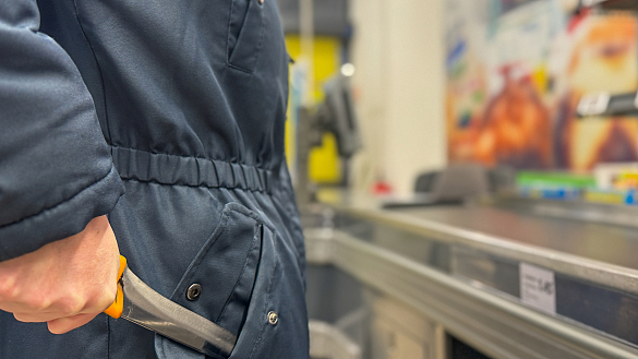 Person, die in Kassenzone steht und ein Messer aus der Jackentasche zückt