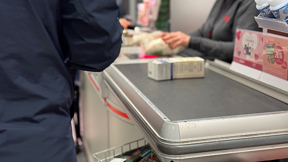 Dunkel gekleidete Person steht im Bereich der Kassenzone eines Supermarktes