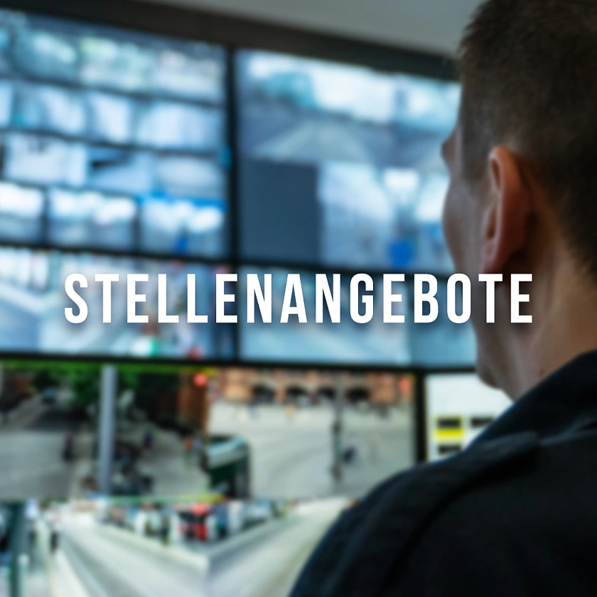 Auf dem Foto ist eine Person zu sehen, die vor einer Wand voller Bildschirmen sitzt