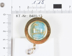 Asservat 1.13: goldener Kettenanhänger mit einen hellblauen Objekt in dem sich goldene Kettenglieder befinden