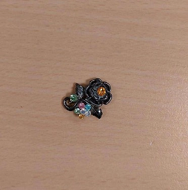 Anstecker in schwarz mit bunten Steinen.