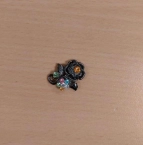 Anstecker in schwarz mit bunten Steinen.