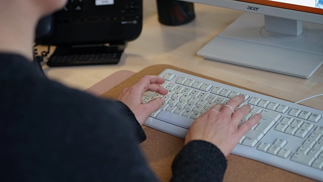 Auf dem Foto ist eine Frau zu sehen, die etwas auf einer Tastatur tippt