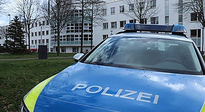 Auf dem Foto ist ein Streifenwagen vor einem weißen Gebäude zu sehen