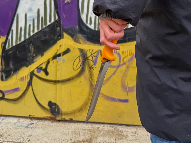 Person steht vor Graffiti Wand und hält ein Messer in der Hand